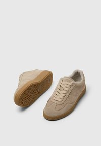 Beżowe zamszowe sneakersy z zaokrąglonym noskiem, teksturowaną cholewką, płaskimi sznurówkami i podeszwą z gumy w kolorze gumy z wzorzystym bieżnikiem.