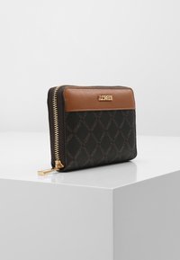 Cartera negra hecha de material sintético texturizado, con un acento de cuero marrón, cremallera dorada y detalle de logo en la parte frontal.