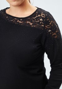Schwarzer Pullover mit einer Spitzenblende und floralen Mustern, kurzen Ärmeln und dezenten Strassverzierungen auf dem Körper.