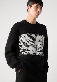 Black knitted sweater featuring a white and gray tiger stripe pattern in the center. Textured fabric, round neckline, and relaxed fit.