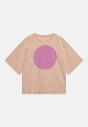 Perzikkleurig oversized t-shirt van zachte katoen, met een grote paarse cirkelvormige grafiek en tekst rondom de rand.