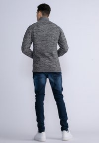 Maglione grigio a trama con colletto alto, orlo a coste e design aderente, abbinato a jeans blu scuro e sneaker bianche.