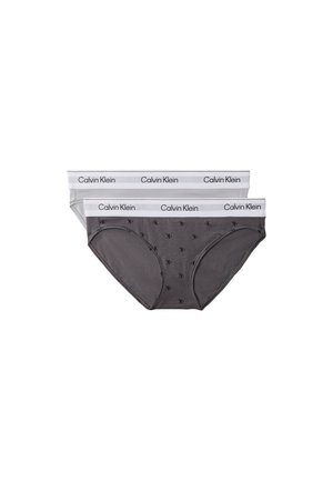 Jeune femme posant en soutien-gorge gris clair Calvin Klein et sous-vêtements assortis sur un fond gris uni.