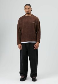 Bruine fleece trui met een ronde hals, lange mouwen en een gestructureerde afwerking. Gecombineerd met loszittende zwarte spijkerbroek en chunky schoenen.