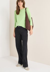 Chemise verte à manches longues, jean noir à jambes larges, sac à bandoulière marron et baskets beige. Design simple avec une texture lisse et des ornements minimalistes.