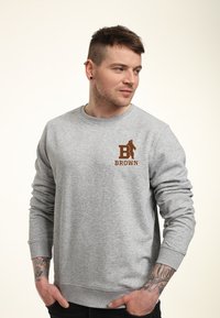 Felpa grigia in misto cotone, con scollatura rotonda e maniche lunghe. Presenta una grafica marrone con la lettera "B" e la scritta "BROWN" sul petto.