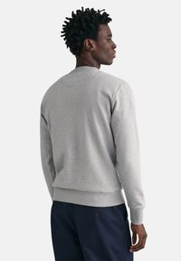 Lichtgrijze sweatshirt met ribgebreide manchetten en zoom, ronde hals en een zachte textuur. Gecombineerd met donkere marineblauwe broek, gezien vanuit de achterkant.