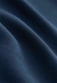 Navy modrý bavlněný materiál s hladkou texturou a jemným žebrováním, s měkkými záhyby zvýrazňujícími splývání a jemnost.