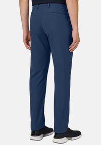 Marineblaue Hose aus leichtem Stoff mit geradem Bein, Gesäßtaschen und kombiniert mit schwarzen Sportschuhen.