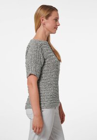 Grijze gebreide trui met een gestructureerd patroon, korte pofmouwen en een wijde halslijn, gecombineerd met lichtgekleurde broek.