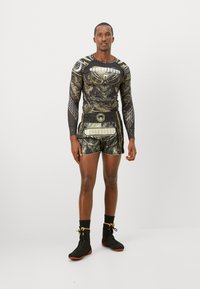 Langærmet sort og guld kompressionsskjorte med grafisk design, parret med matchende shorts. Tekstureret stof, atletisk pasform og kontrasterende detaljer.
