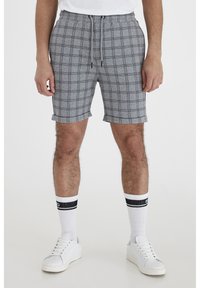 Shorts en tartan gris avec une taille élastique et un cordon de serrage, présentant des poignets roulés. Associés à des baskets blanches et des chaussettes rayées.