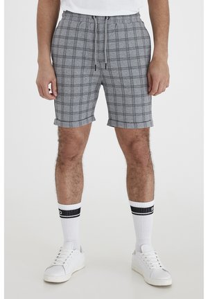 Grå ternede shorts med elastisk talje og snoretræk, med optrukne manchetter. Kombineret med hvide sneakers og stribede sokker.