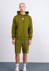Felpa verde oliva con coulisse regolabili e logo, abbinata a pantaloni corti coordinati. Tessuto morbido, vestibilità rilassata e polsini a costine.