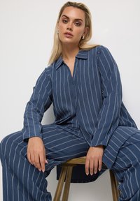 Camicia a maniche lunghe a righe blu con colletto e chiusura con bottoni, abbinata a pantaloni a gamba larga coordinati. Tessuto morbido, vestibilità casual.