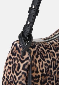 Handbag z leopardskim vzorcem s puhasto teksturo, črnimi usnjenimi detajli in zadrgo. Ima trak z detajli iz srebrne kovine.