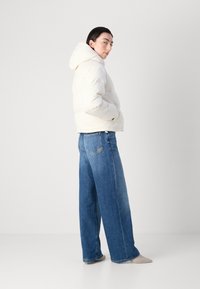 Hvit pufferjakke med hette, med en quiltet design. Kombinert med vide blå jeans og beige sko. Glatt tekstur og uformell passform.