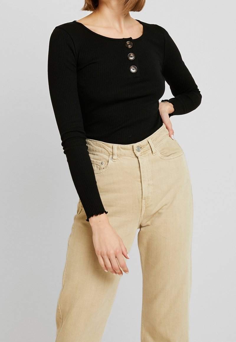 Zwarte geribbelde langlijns t-shirt met een ronde halslijn en een vierknops placket, gecombineerd met beige high-waisted jeans. Geëtrukt stof.