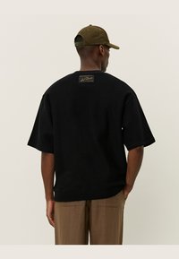 Tricou scurt cu mânecă, din tricot negru, cu material texturat și croială pătrată. Dispune de o etichetă de marcă pe spate și tiv ribat.