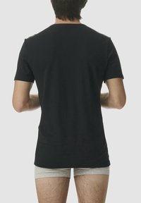 T-shirt nero a maniche corte in cotone, con forma aderente, texture liscia, vista da dietro, indossato con biancheria intima grigia chiara.