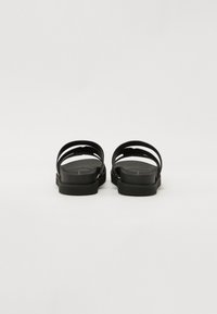 Schwarze flache Sandalen mit minimalistischem Design, ausgestattet mit zwei breiten Riemen, einer glatten matten Oberfläche und einer strukturierten Sohle für besseren Halt.