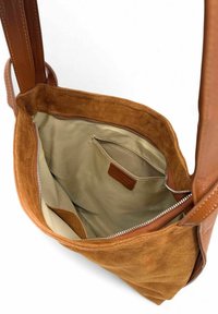 Sac à épaule en suède tan avec des poignées en cuir, fermeture éclair et un intérieur beige doublé comprenant une poche latérale et un détail de texture en tissu.