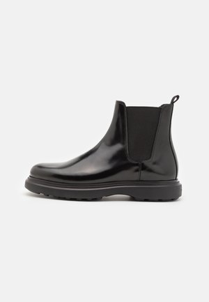 Bottines Chelsea noires en cuir brillant avec des panneaux latéraux élastiques, une languette à l'arrière et une semelle robuste pour une bonne adhérence.