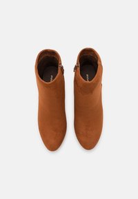 Bottines en suède marron avec une texture lisse, fermeture éclair sur le côté et une silhouette élégante.