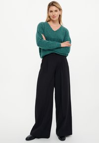 Groene v-hals trui van zacht materiaal, gecombineerd met hoge taille, wijde zwarte broek. De trui heeft losse mouwen en een ontspannen pasvorm.