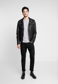 Black leather motorcycle jacket with silver zippers, grey fitted t-shirt, black jeans, and black ankle boots, standing against a plain background.