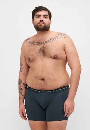 Dunkelgraue Boxershorts mit einem elastischen Bund, auf dem der Markenname 'JACK & JONES' steht. Das Modell hat kurze Haare und sichtbare Tattoos.