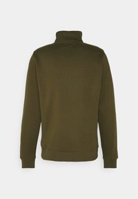 Dunkel olivgrüner Pullover. Verfügt über einen hohen Kragen, lange Ärmel sowie gerippte Bündchen und Saum. Weicher Stoff mit minimalen Designdetails.