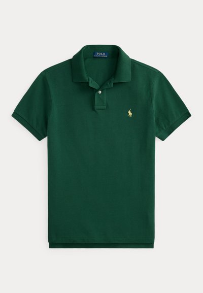 Πράσινο σκούρο κοντομάνικο πόλο μπλουζάκι με γιακά, δύο κουμπιά στο πέτο και μικρό χρυσό κεντητό λογότυπο παίκτη πόλο στο αριστερό στήθος.