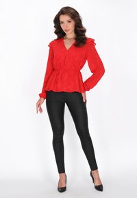 Punainen pitkähiha blouse, jossa on röyhelövuoret ja peplum-vyötärö, yhdistettynä tiukkoihin mustiin legginsseihin ja mustiin kärjellisiin korkokenkiin.