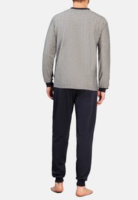 Graues Langarmshirt mit einem strukturierten Muster, kombiniert mit dunklen Marineblauen Hosen, die beide eng anliegenden Manschetten und einen entspannen Schnitt aufweisen. Keine Schuhe.