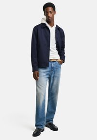 Chaqueta azul marino con cierre de botón, sudadera blanca debajo, jeans de color azul claro y zapatos negros. Textura suave, diseño casual.
