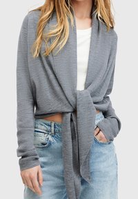 Szary, żeberkowany, krótszy kardigan z zapięciem na sznurek. Posiada długie rękawy i luźny krój, zestawiony z jasnoniebieskimi dżinsami.