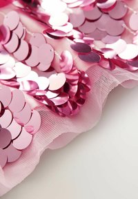 Paillettes rotonde lucide rosa cucite su tessuto rosa morbido e trasparente con trama a rete, disposte in file sovrapposte creando una superficie riflettente.