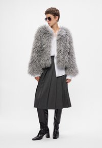 Skrócona kurtka z futra syntetycznego w kolorze szarym, biała koszula z guzikami, plisowana szara spódnica midi oraz czarne kozaki na wysokim obcasie do kolan; modelka nosi okulary przeciwsłoneczne.