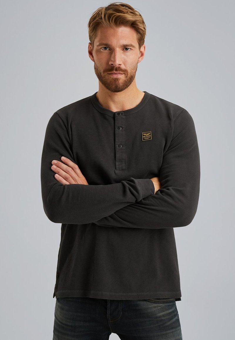 Langärmliges schwarzes Henley-Shirt mit drei Knöpfen und einem kleinen rechteckigen Logo-Patch auf der Brust. Weicher Stoff mit lässiger Passform.
