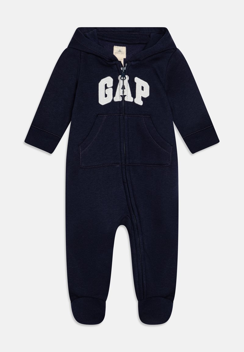 Tamnoplav onesie na zip z kapuco, belim logotipom "GAP", dvema sprednjima žepoma ter rebrastimi manšetami na gležnjih in zapestjih. Mehka tkanina.