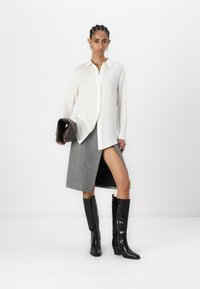 Camisa branca, saia cinza à frente e botas altas pretas. O conjunto apresenta um tecido texturizado e uma mala estruturada, com um design elegante.