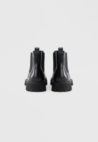 Mustat nilkkurit, joissa on sileä nahkapinta, joustavat sivupaneelit ja paksut kumipohjat syvillä urilla paremman pidon takaamiseksi.