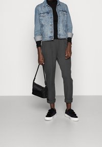 Jeansjacke in Hellblau, schwarzes Langarmshirt, graue maßgeschneiderte Hose, schwarze Umhängetasche und schwarze Sneaker mit weißen Sohlen.