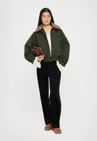 Olive zaļa īsa jaka ar leoparda raksta vilnas apkakli, pārī ar krēmkrāsas topu, melnām korduroja biksēm un brūniem platformas apaviem.