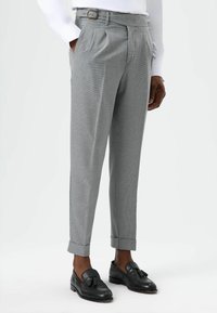 Grijze geruite broek met een geplooide voorkant, voorzien van een riemlus en omgeslagen zoom, gecombineerd met zwarte loafers. Gladde textuur en een getailleerde pasvorm.