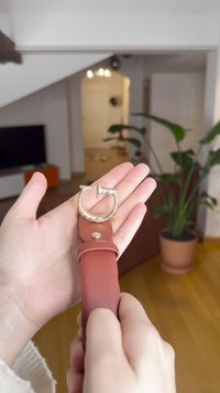 Bracelet en cuir avec une boucle en métal doré incurvée. La sangle est d'un brun rougeâtre riche avec une texture lisse et un élément de design circulaire.