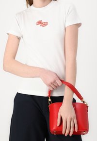 Hvid t-shirt med rødt logo, parret med en lille rød håndtaske med et strømlinet design og guld hardware detaljer.