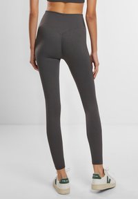 Høyt midjete, ribbestrikkede leggings i mørkegrått, med en v-formet søm bak. Kombinert med hvite sneakers med grønne detaljer.