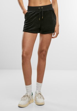 Zwarte fluwelen shorts met een drawstring tailleband, voorzien van gouden accenten, zijzakken en een relaxte pasvorm. Gestyled met witte sneakers en sokken.